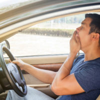 Asian young man driving a car and feel sleepy.