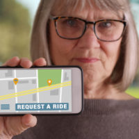 Mature white female holding up smartphone to camera with rideshare app open Mature white female holding up smartphone to camera with rideshare app open