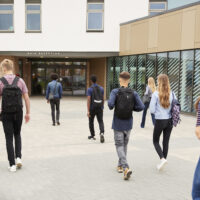 Rear View Of High School Students Walking Into College Building Together Rear View Of High School Students Walking Into College Building Together