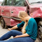 Upset driver woman in front of automobile crash car.