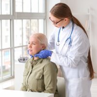 Doctor examining senior woman with thyroid gland problem in clin Doctor examining senior woman with thyroid gland problem in clin