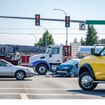 Damaged cars after a car accident crash involving a big rig semi truck with semi trailer at a city street crossroad intersection with traffic light and rescue services to help the injured