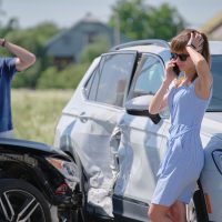 Angry woman and man drivers of heavily damaged vehicles calling insurance service for help in car crash accident on street side.