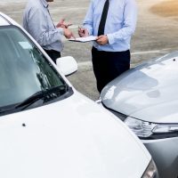 Insurance agent writing on clipboard while examining car after accident claim being assessed and processed