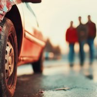 Red damaged car parked on the roadside after a road accident with people leaving the scene