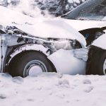 Close up view of a car crash on a snowy road in winter, where two white cars have been wrecked in a front collision