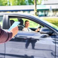Taxi phone app for cab or car ride share service. Customer waiting driver to pick up on city street. Man holding smartphone. Mobile and online booking for rideshare transportation with cellphone.