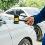 A lawyer stands next to a car, holding a gavel symbolizing legal authority and judgment. The scene depicts legal representation and consultation in matters related to automobile law.