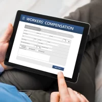 a-person-in-business-attire-holds-a-tablet-displaying-a-workers-compensation-form